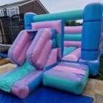 A Pastel Coloured bouncy castle with front facing slide side view
